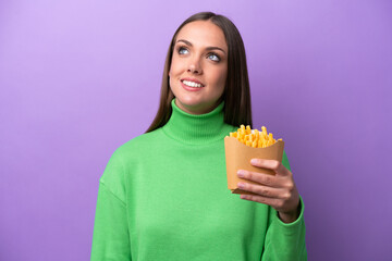 Young caucasian woman holding fried chips on purple background thinking an idea while looking up