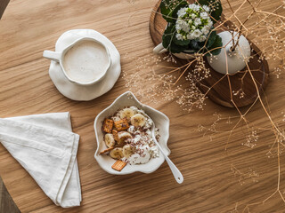 Delicious breakfast, brunch - cottage cheese with banana, sour cream, crackers, chocolate and cappuccino on a round wooden table, top view - 783615193