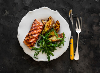 Delicious lunch - grilled salmon, baked potatoes and arugula salad on a dark background, top view - 783615718