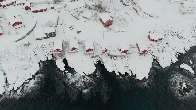 Drohnenaufnahme von Hamnoy, rote H&auml;user mit schneebedeckten D&auml;chern, Felsen schimmern unterhalb der t&uuml;rkischen Wasseroberfl&auml;che