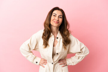 Middle aged caucasian woman isolated on pink background posing with arms at hip and smiling