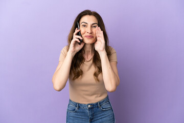 Middle aged caucasian woman using mobile phone isolated on purple background shouting with mouth wide open