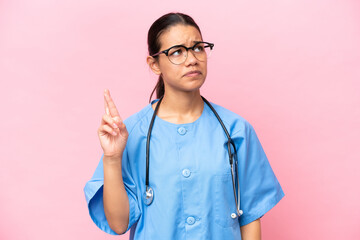 Young nurse Colombian woman isolated on pink background with fingers crossing and wishing the best