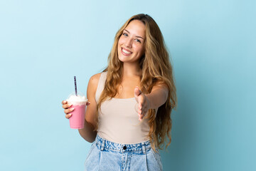 Young woman with strawberry milkshake isolated on blue background shaking hands for closing a good...