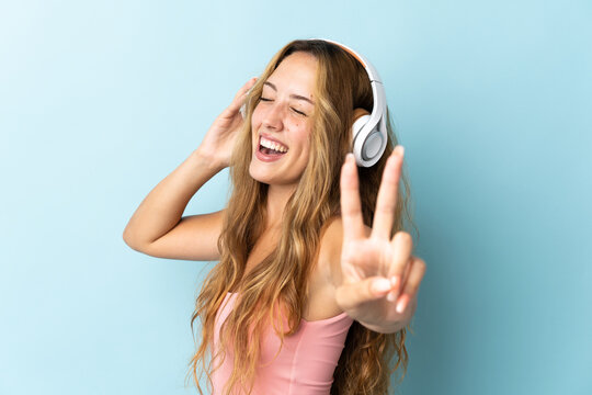 Young blonde woman isolated on blue background listening music and singing