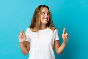 Young blonde woman isolated on blue background with fingers crossing