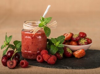Closeup shot of a juicy red smoothie near a bunch of cherries, raspberries, and strawberries