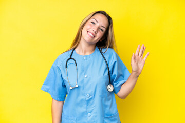Young surgeon nurse woman isolated on yellow background saluting with hand with happy expression