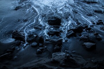 Waves moving to the dark blue seashore covered with rocks - Powered by Adobe