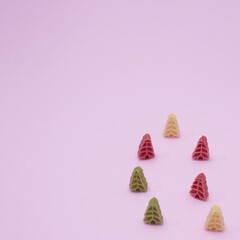High-angle view of colorful pasta in the shape of Christmas trees on a pink background