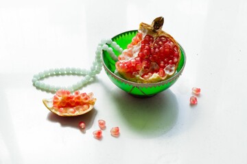 Sliced pomegranate in a small green bowl next to white beads