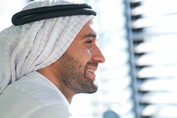 Profile of a smiling man in traditional Emirati attire, his face lit by the warmth of sunlight,...