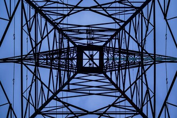 Low-angle shot from below a high-voltage electricity tower with the blue sky in the background