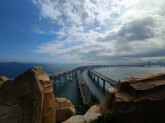 Aerial view of the Xinghaiwan Bridge over the sea in Dalian, China on a sunny day - obrazy, fototapety, plakaty