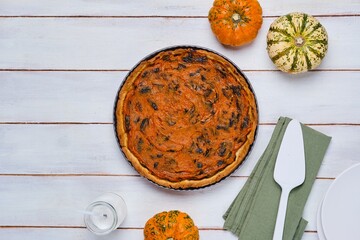 Round tart with pumpkin and prunes in the form for baking on a light derving background. Pumpkin recipes. French cuisine.