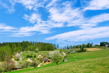 View of the surrounding countryside with hills, houses, meadows and a forest under a blue sky and mountain Malnik in summer spring day, Muszyna, Beskid Sadecki, Poland