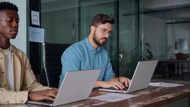 Two busy diverse business men company employees using laptops working in office. Professional young businessmen colleagues workers typing on computer technology at office workplace desk.