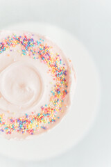 Vertical top view of a light pink cake with sprinkles on white background