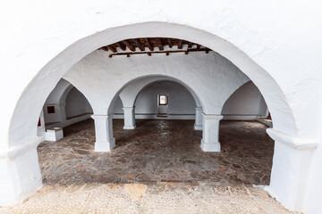 Inside Puig de Missa, a covered courtyard reveals a serene sequence of white arches and columns,...