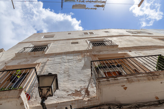 Looking up at an old, weathered house in Eivissa historic town, Ibiza, Spain, its facade telling stories of time with peeling paint and rustic balconies against a blue sky