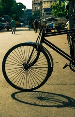 Vertical closeup of a bicycle front wheel on the roadside with walking people background