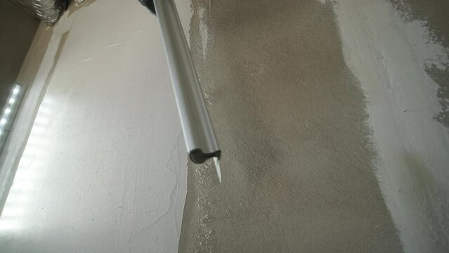 Close-up view of a worker's arm installing a metal corner bead on a drywall to protect and define the edge of the plasterwork