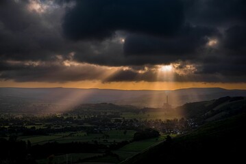 Drone view of nature with green fields and houses under a cloudy sky illuminated by small sun rays