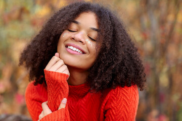 Young happy overjoyed african american woman with curly hair keeping eyes closed laughing and having fun while standing in autumn forest
