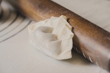 Closeup of a homemade stuffed dumpling near a rolling pin on a kitchen table