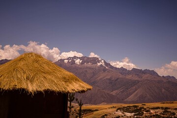 The straw roof of a hut against the backdrop of a mountain range on a sunny day