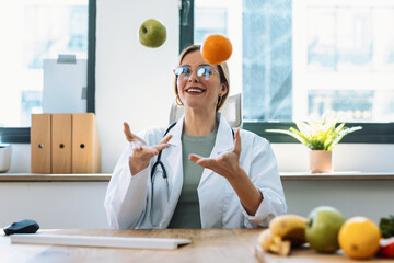 Beautiful young woman nutritionist having fun while juggling an apple and an orange on a nutritionist consultation