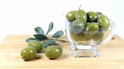Closeup shot of green olives and an olive tree branch on a wooden board