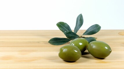 Closeup shot of green olives and an olive tree branch on a wooden board