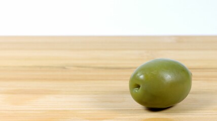 Closeup shot of a green olive on a wooden board