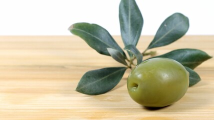 Closeup shot of a green olive and an olive tree branch on a wooden board