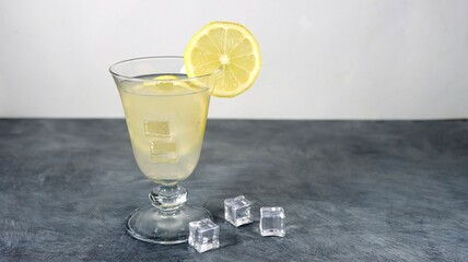 Glass with a gin lemon cocktail and icecubes on a gray table