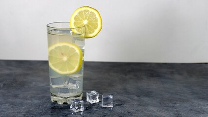 Glass with a gin lemon cocktail and icecubes on a gray table