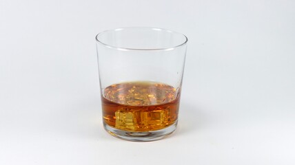 Glass with brown liquid and square ice cubes on a white background