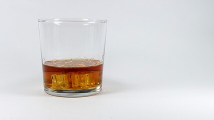 Glass with brown liquid and square ice cubes on a white background