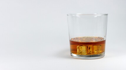 Glass with brown liquid and square ice cubes on a white background