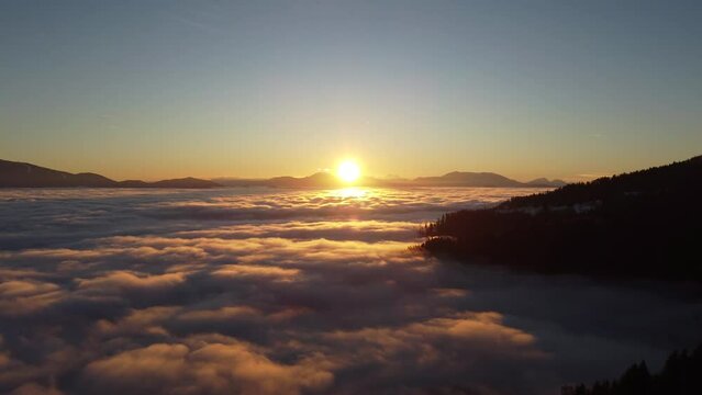 Aerial of low clouds and mountains with the golden sunset shining in the background