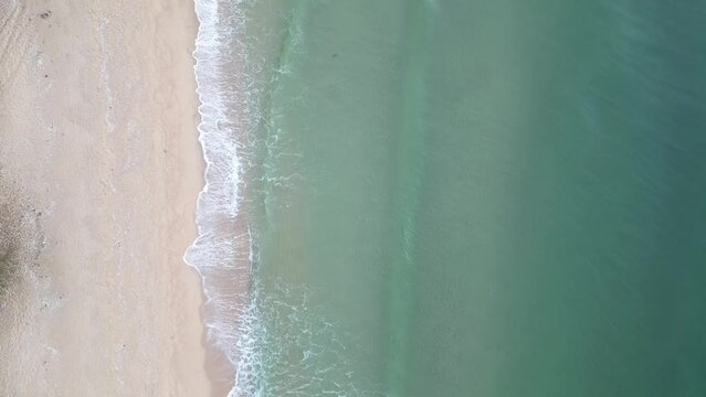 Aerial view of a sandy beach with waves. An aerial top view of a beautiful sight as turquoise ocean waves break the beach's sandy shoreline and white foam waves.
