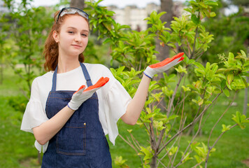 Front view of young female florist standing, gardening, showing, looking at camera. Concept of taking care of plants.