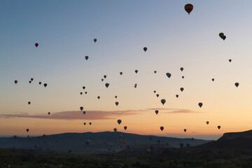 Dozens of hot air balloons rising over the landscape of the Red Valley, Rose Valley before sunrise, close to Goreme, Cavusin, Cappadocia, Turkey