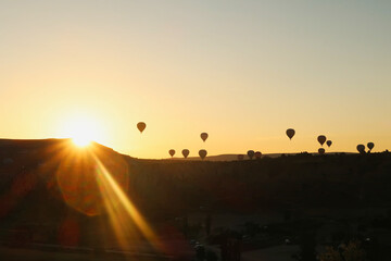 Hot air balloons coming over the edge of a hill where the sun is about to rise, Göreme view point,...