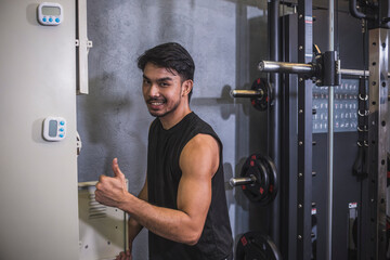 A fit Asian man with a positive thumbs up gesture standing by a locker at a gym, showcasing a...