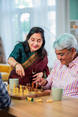 Mature Indian couple enjoying while playing chess board game together at home.