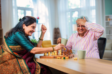 Mature Indian couple enjoying while playing chess board game together at home.