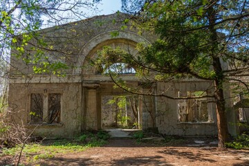 facade of an old abandoned dilapidated villa surrounded by the first spring bright green foliage in an abandoned park on the Black Sea coast on a sunny day in April