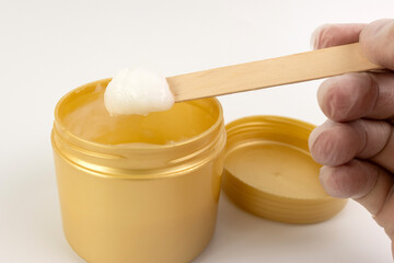 A cosmetic gel from a plastic jar is applied to a wooden spatula.